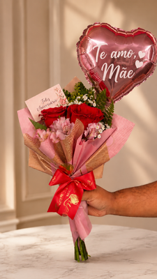 Arranjo com rosas vermelhas, folhagens verdes, embalagem em tons de rosa e dourado, laço vermelho e cartão de aniversário.